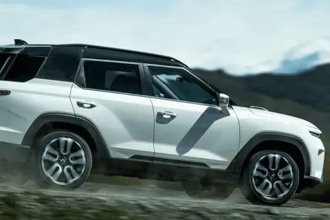 Biały SUV torres auto pokonuje wyboistą drogę, wzbijając tumany kurzu. W tle górzysty, surowy krajobraz.