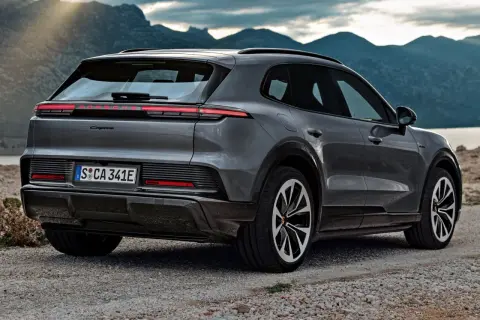 Nowe Porsche Cayenne w szarym kolorze, zaparkowane na kamienistej drodze z widokiem na góry i jezioro.