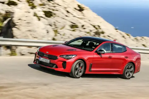 Czerwony Kia Stinger pędzi po krętej drodze nad morzem.