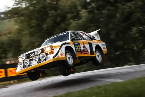 Audi Sport Quattro w akcji, pokonuje nierówność drogi, unosząc się w powietrzu.