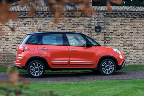 Pomarańczowy Fiat 500 XL z czarnym dachem zaparkowany przy ceglanej ścianie.