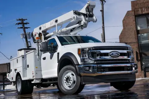 Biały Ford F650 z podnośnikiem koszowym, gotowy do pracy przy liniach energetycznych.