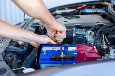 Ręce mechanika dokręcają klemę akumulatora. Widać silnik i elementy instalacji elektrycznej, czuć napięcie przed uruchomieniem.