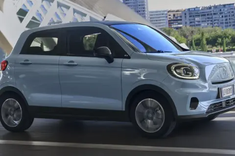Jasnoniebieski Leapmotor T03 jedzie po drodze, z nowoczesną architekturą w tle.