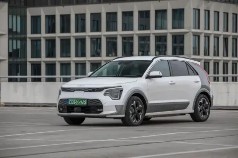 Biała Kia Niro na parkingu, z nowoczesnym budynkiem w tle. Sprawdź kia niro wymiary, by poznać jej kompaktową sylwetkę.