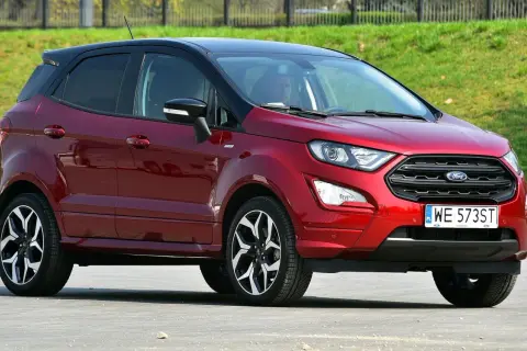 Czerwony Ford EcoSport z czarnym dachem, zaparkowany na tle zielonego zbocza.