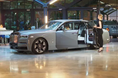 Elegancki szary Rolls-Royce Phantom z otwartymi drzwiami, obok stoi kobieta. Poznaj jego imponującą rolls royce cena.