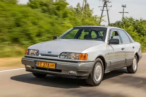 Srebrny Ford Scorpio z lat 90. pędzi po wiejskiej drodze, otoczony zielenią.