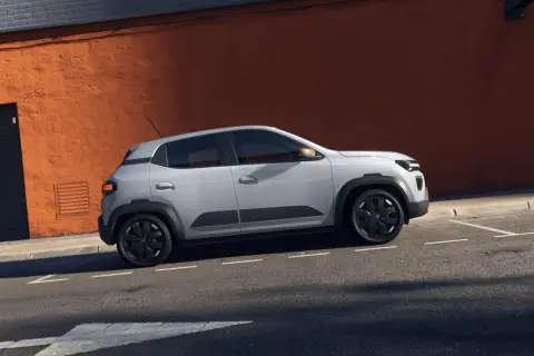 Jasnoszary Dacia Spring na tle pomarańczowej ściany. Sprawdź atrakcyjną dacia spring cena i odkryj jego zalety.