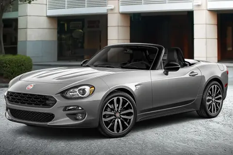 Szary Fiat Spider z czarnym dachem, zaparkowany przed budynkiem.