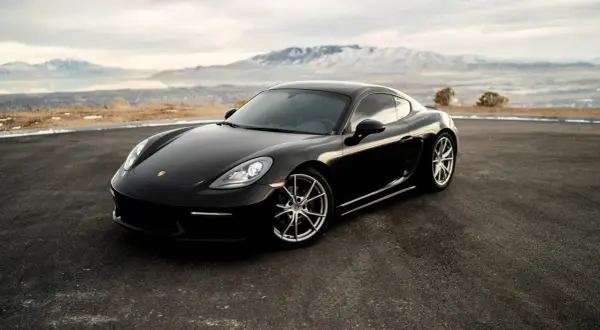Czarny Porsche Cayman na tle gór i jeziora. Zastanawiasz się, ile kosztuje Porsche?
