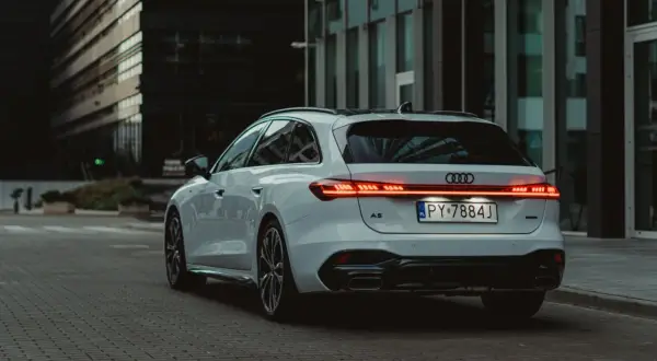 Białe Audi A5 Avant 2025 z nowoczesnym pasem świateł LED na klapie bagażnika, zaparkowane na tle szklanych budynków.