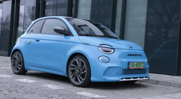 Niebieski Abarth 500e, gotowy do testu, zaparkowany przed nowoczesnym budynkiem.