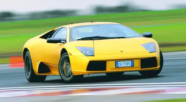 Żółty Lamborghini Murcielago pędzi po torze wyścigowym, zostawiając za sobą rozmyte zielone krajobrazy.