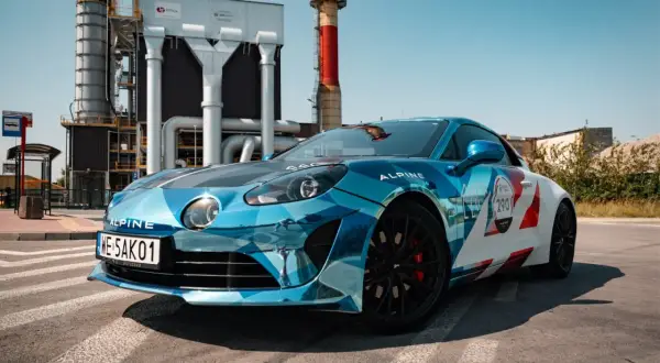 Błękitno-białe Alpine A110S z numerem 290 na tle przemysłowej zabudowy.