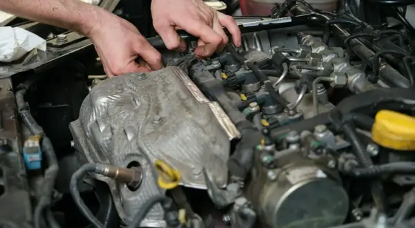 Mechanik pracuje przy silniku, wymieniając czujnik położenia wałka rozrządu.