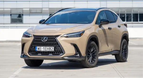 Elegancki, beżowy Lexus 350h z czarnym dachem i felgami stoi na parkingu przed nowoczesnym budynkiem.