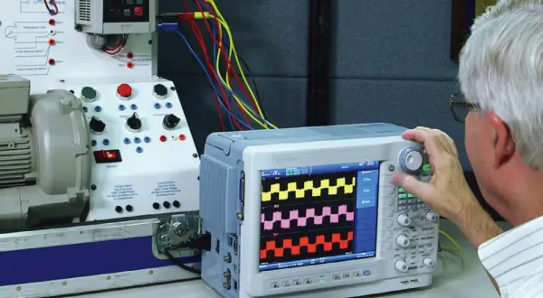 Mężczyzna reguluje oscyloskop, który pokazuje przebiegi, pomagając zrozumieć, jak zmierzyć moc silnika elektrycznego.