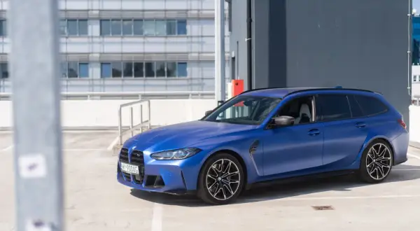 Niebieskie BMW M3 Touring na parkingu. Sportowy kombi z charakterystycznymi felgami i matowym lakierem.