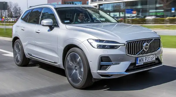 Srebrny Volvo XC60 T6 w ruchu miejskim, z kierowcą za kierownicą. Elegancki SUV na tle nowoczesnych budynków.