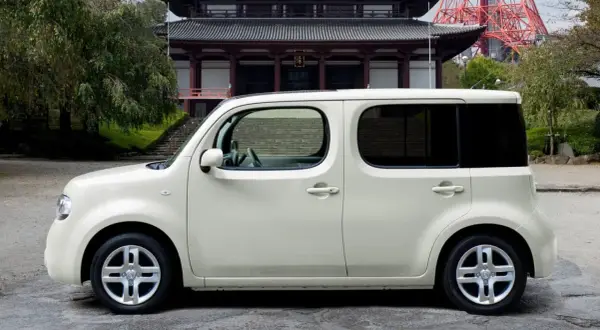 Biały Nissan Cube zaparkowany przed tradycyjną japońską świątynią.