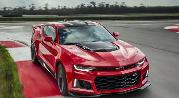 Czerwone Camaro ZL1 z czarnymi pasami pędzi po torze wyścigowym, zostawiając za sobą smugę prędkości.