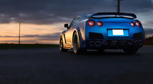 Niebieski Nissan GTR z charakterystycznymi światłami z tyłu, zaparkowany o zachodzie słońca. Zastanawiasz się nad nissan gtr cena?