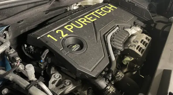 Silnik 1.2 PureTech, często chwalony w opiniach za oszczędność. Widok z bliska na pokrywę silnika z żółtym napisem.