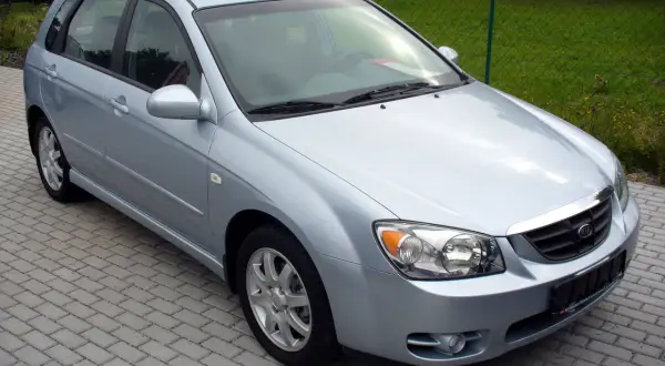 Jasnosrebrny Kia Cerato hatchback stoi na chodniku z kostki brukowej.