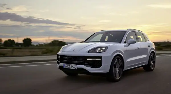 Biały Porsche Cayenne Turbo sunie po drodze o zachodzie słońca, z chmurami malującymi niebo.