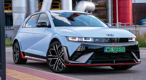 Niebieski Hyundai Ioniq 5 N z czerwonymi akcentami stoi przed przemysłowym budynkiem z rurami.