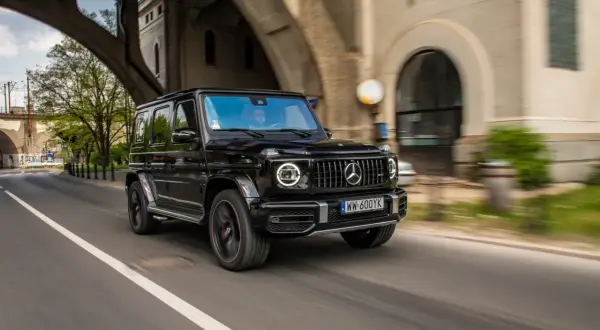 Czarny G-wagon pędzi pod wiaduktem, kierowca w okularach obserwuje drogę.