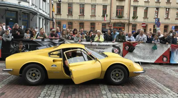 Żółte Ferrari Dino z otwartymi drzwiami, kierowca w środku, tłum widzów za barierką.