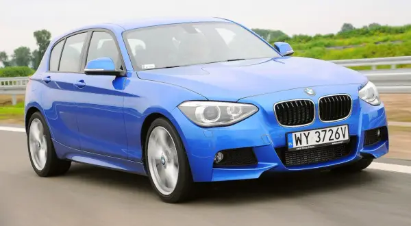Niebieskie BMW 116i pędzi po drodze, ukazując swoje sportowe linie i dynamiczny charakter.