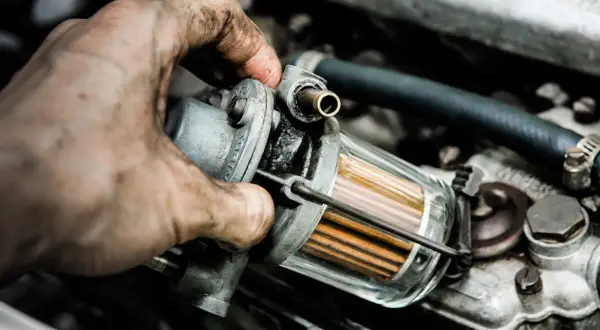 Brudna ręka mechanika wymienia jeden z filtrów w instalacji LPG. Widać przezroczysty korpus filtra z pomarańczowymi wkładami.