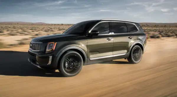 Ciemnozielony Kia Telluride przemierza pustynną drogę, unosząc kurz.