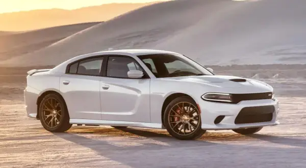 Biały Dodge Charger SRT z brązowymi felgami na pustyni o zachodzie słońca.
