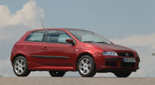 Czerwony Fiat Stilo 1.9 JTD z felgami aluminiowymi stoi na tle błękitnego nieba z chmurami.