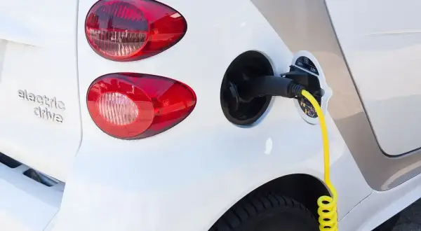 Biały samochód elektryczny z podłączonym żółtym kablem do ładowania.