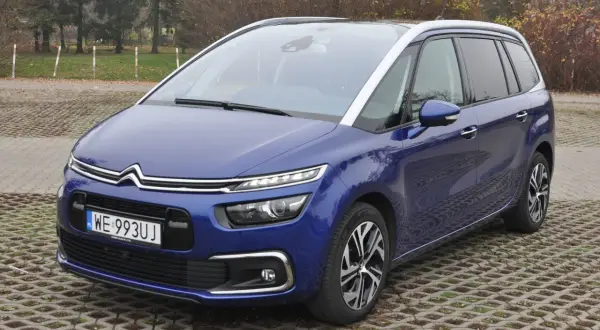 Niebieski Citroen C4 Spacetourer zaparkowany na betonowej nawierzchni z trawą.