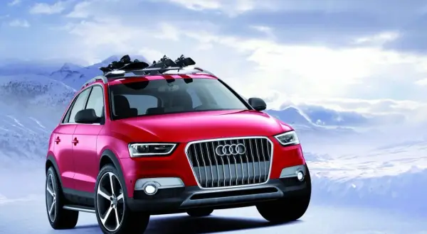 Czerwony Audi Q1 z nartami na dachu gotowy na zimową przygodę w górach.
