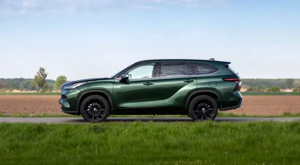 Zielony Toyota Grand Highlander z czarnymi felgami na tle pól i nieba.