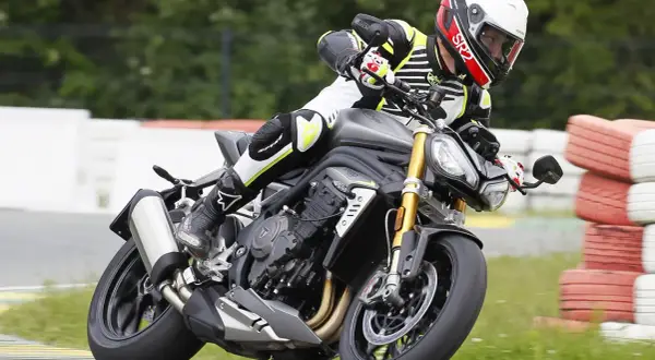 Motocyklista w kasku i kombinezonie pochyla się na torze wyścigowym na motocyklu Triumph Speed Triple.