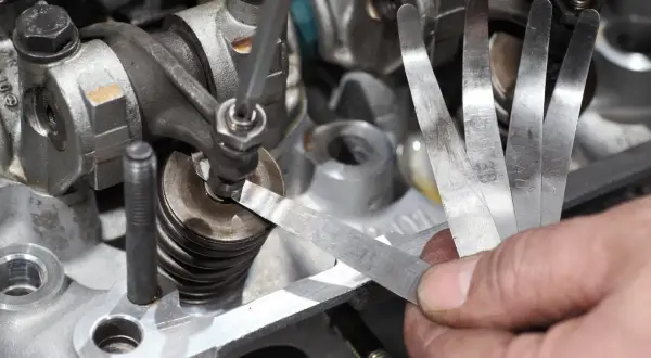Mechanik sprawdza luzy zaworowe za pomocą szczelinomierza w silniku samochodowym.