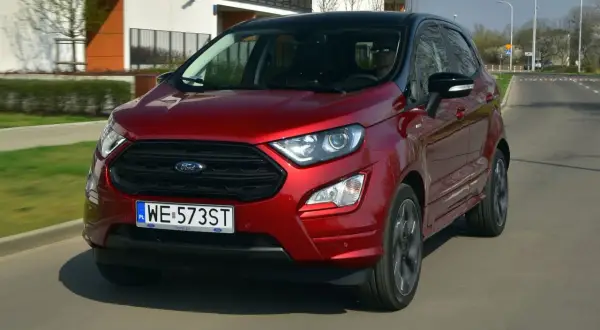 Czerwony Ford Ecosport z czarnym dachem jedzie po miejskiej drodze.