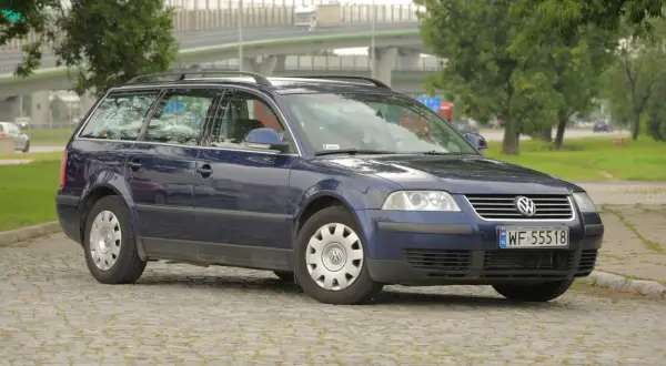 Ciemnoniebieski Volkswagen Passat kombi, model b5, stoi na brukowanym placu.