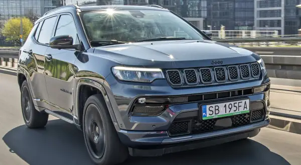 Ciemnoszary Jeep Compass 2025 na drodze, z nowoczesnymi budynkami w tle.