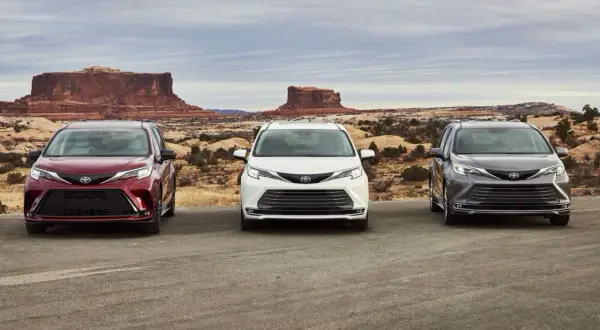 Trzy samochody Toyota Sienna w kolorach: wiśniowym, białym i grafitowym, stoją na tle pustynnego krajobrazu z formacjami skalnymi.
