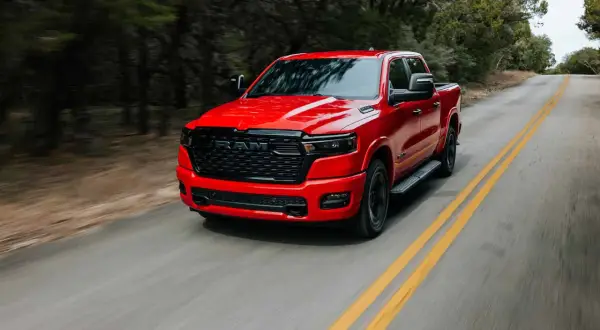 Czerwony Dodge Ram 1500 5.7 Hemi pędzi po krętej drodze wśród drzew.