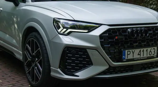 Srebrne Audi RS Q3 z czarnymi felgami i agresywnym grillem, gotowe do jazdy po warszawskich ulicach.